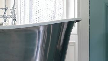 A bathroom with a freestanding bathtub, a window with sheer curtains, and a patterned wall.