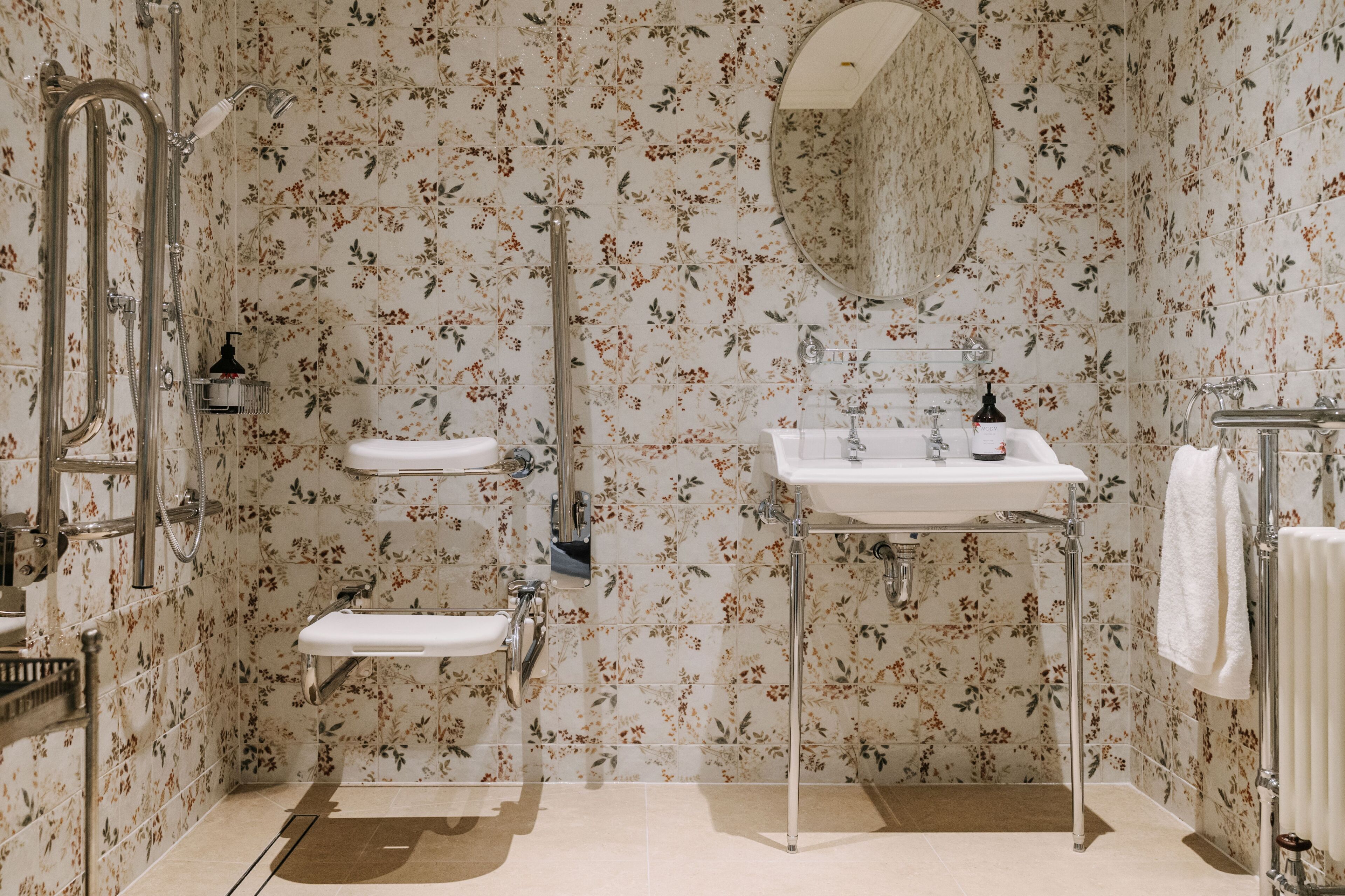 A bathroom with floral wallpaper, a shower, a sink, and a mirror.