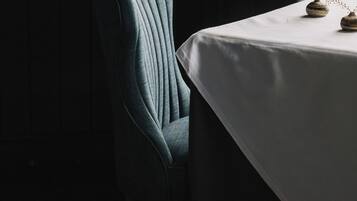 Un comedor con una mesa preparada para dos, una silla y un jarrón con flores secas.