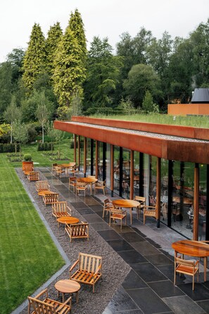 A modern outdoor seating area with wooden furniture and a glass enclosure. - Cromlix (Dunblane)