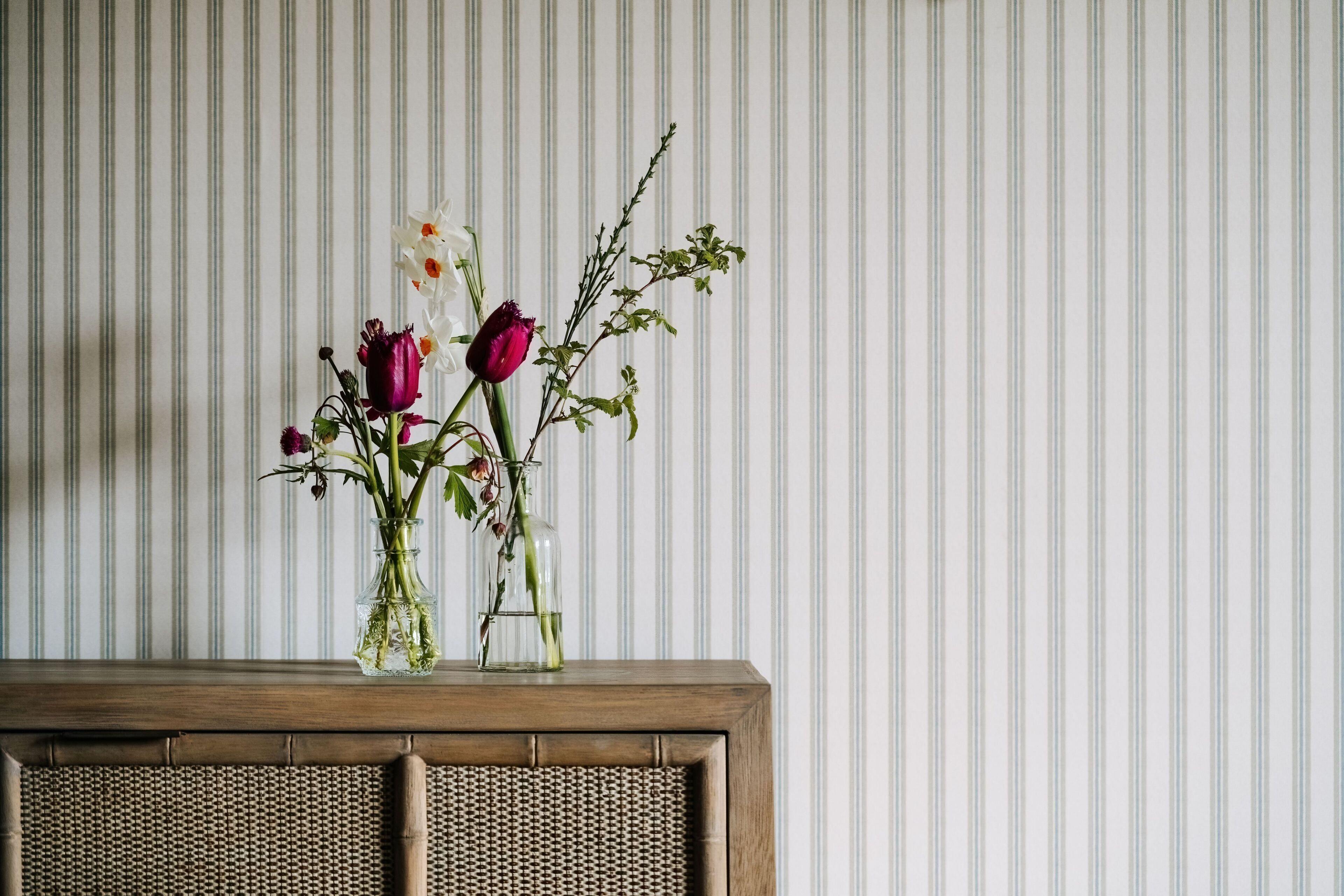 Una mesa de madera con un florero de flores sobre un fondo de papel tapiz a rayas.