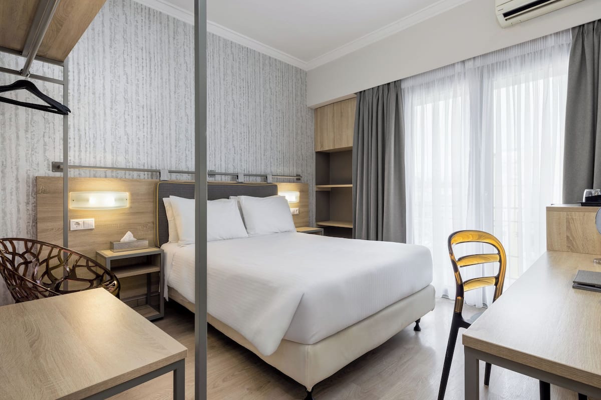 A hotel room with a large bed, bedside tables, a desk, and a chair.