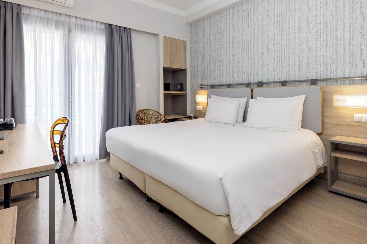 A hotel room with a large bed, a desk, a chair, and a wardrobe.