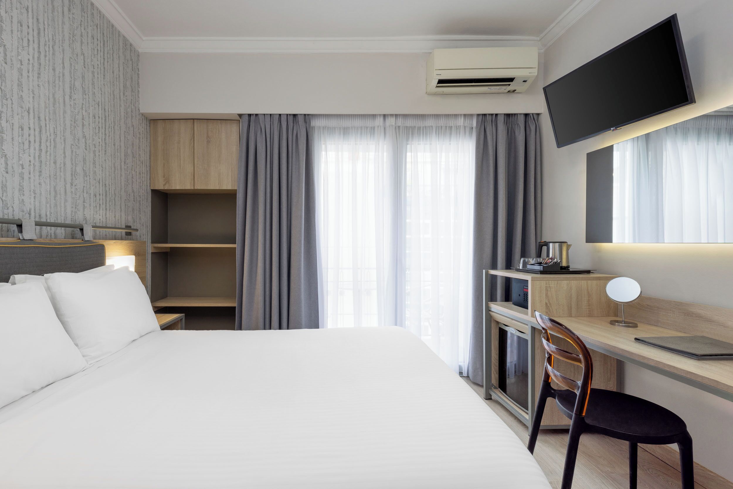 A hotel room with a bed, a desk, a chair, a TV, and a wardrobe.