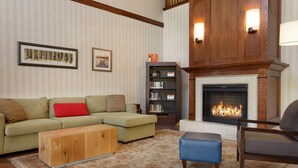 A living room with a sectional sofa, a wooden coffee table, a blue ottoman, a fireplace, and a bookshelf. - Country Inn & Suites by Radisson, Norman near University (Norman)