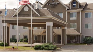 A Country Inn & Suites building with a covered entrance, multiple windows, and a flagpole with an American flag. - Country Inn & Suites by Radisson, Norman near University (Norman)