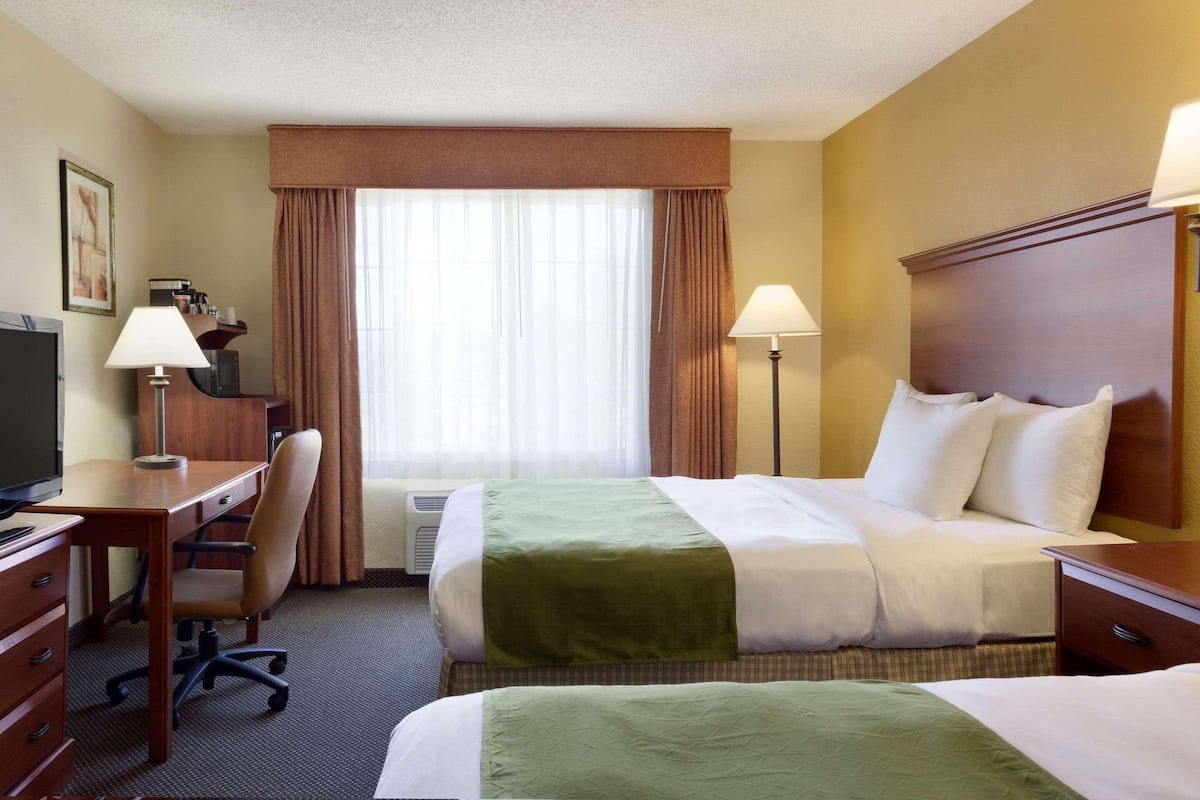 A hotel room with two beds, a desk, a chair, and a television.