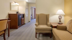 A hotel room with a wooden bench, a striped armchair, a sofa, a small table with a lamp, a minibar, and a mirror on the wall. - Country Inn & Suites by Radisson, Norman near University (Norman)