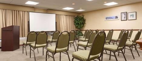 Une salle de conférence équipée d’un pupitre, d’un grand écran et de plusieurs chaises disposées en rangées.