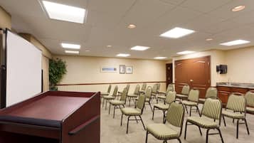 A conference room with a long table, rows of chairs, a projector screen, and a door.