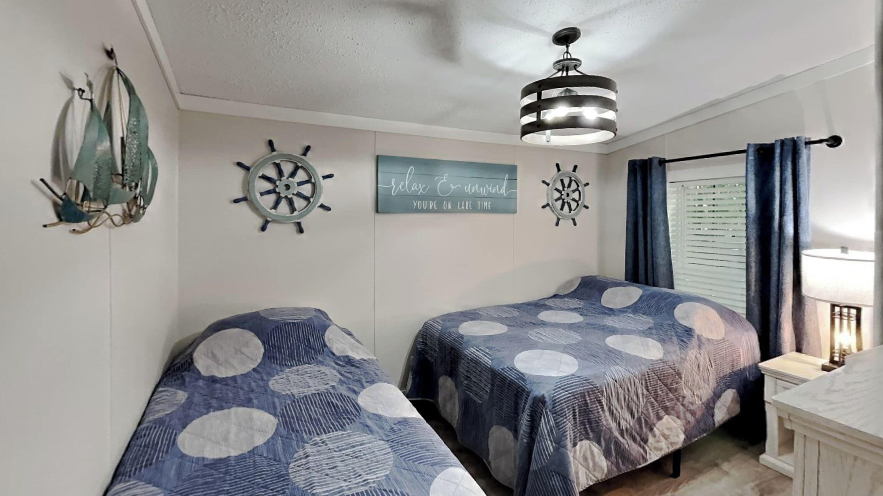 A bedroom with two beds, nautical decor, a ceiling fan, and a window with curtains.