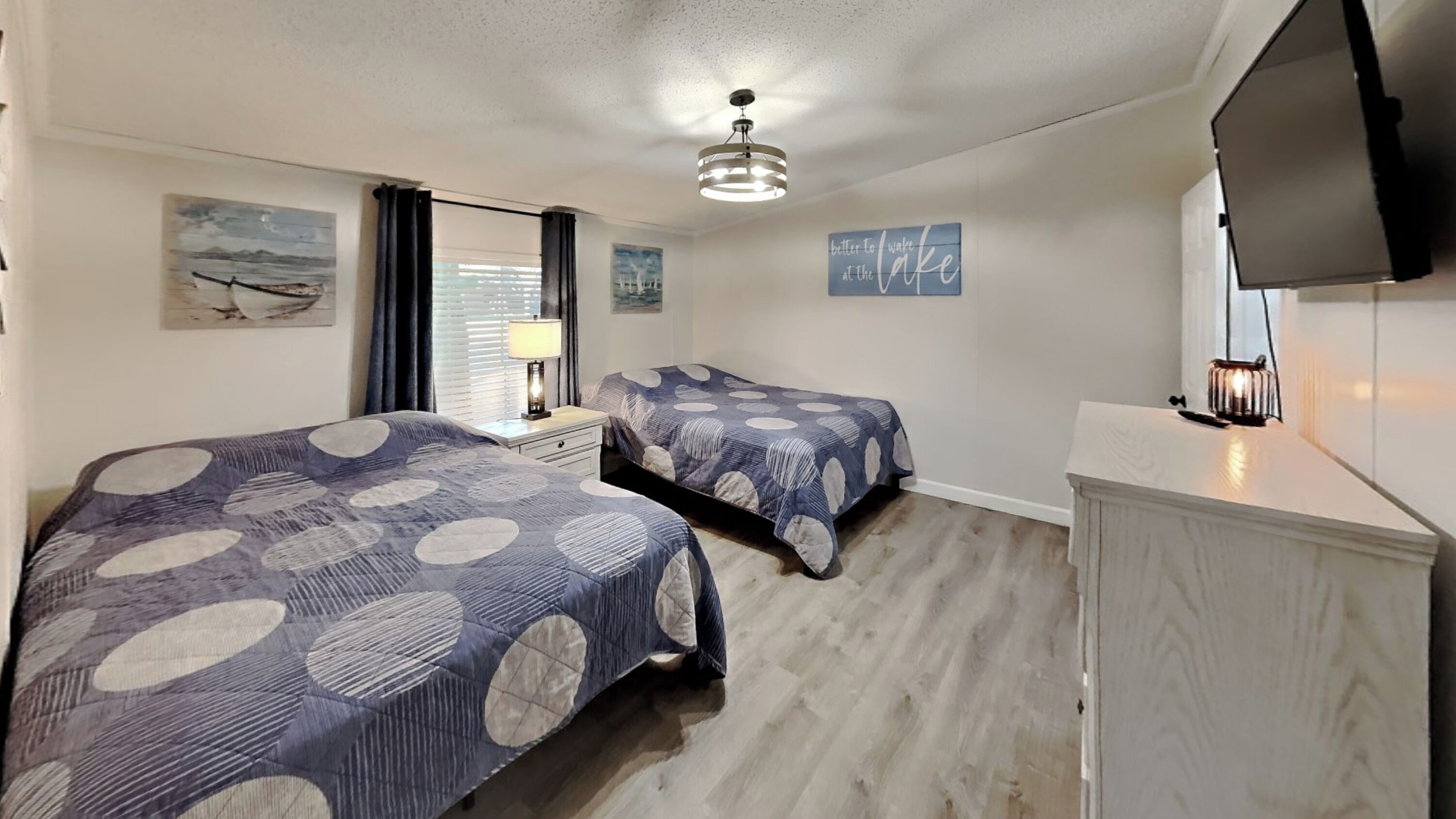 A bedroom with two beds, a nightstand, a lamp, a television, and artwork on the walls.