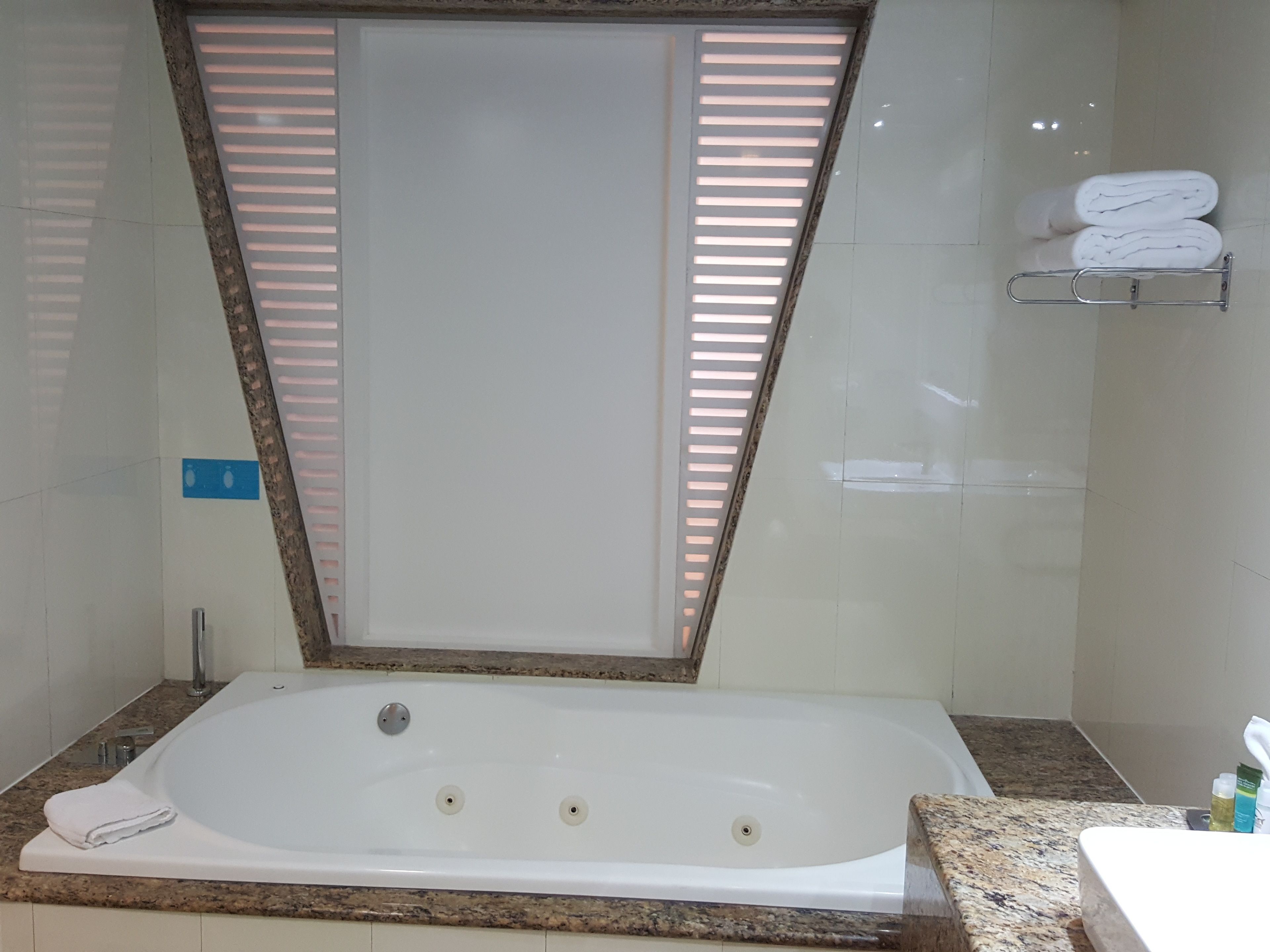 A modern bathroom with a freestanding bathtub, a towel rack with folded towels, and a window with blinds.