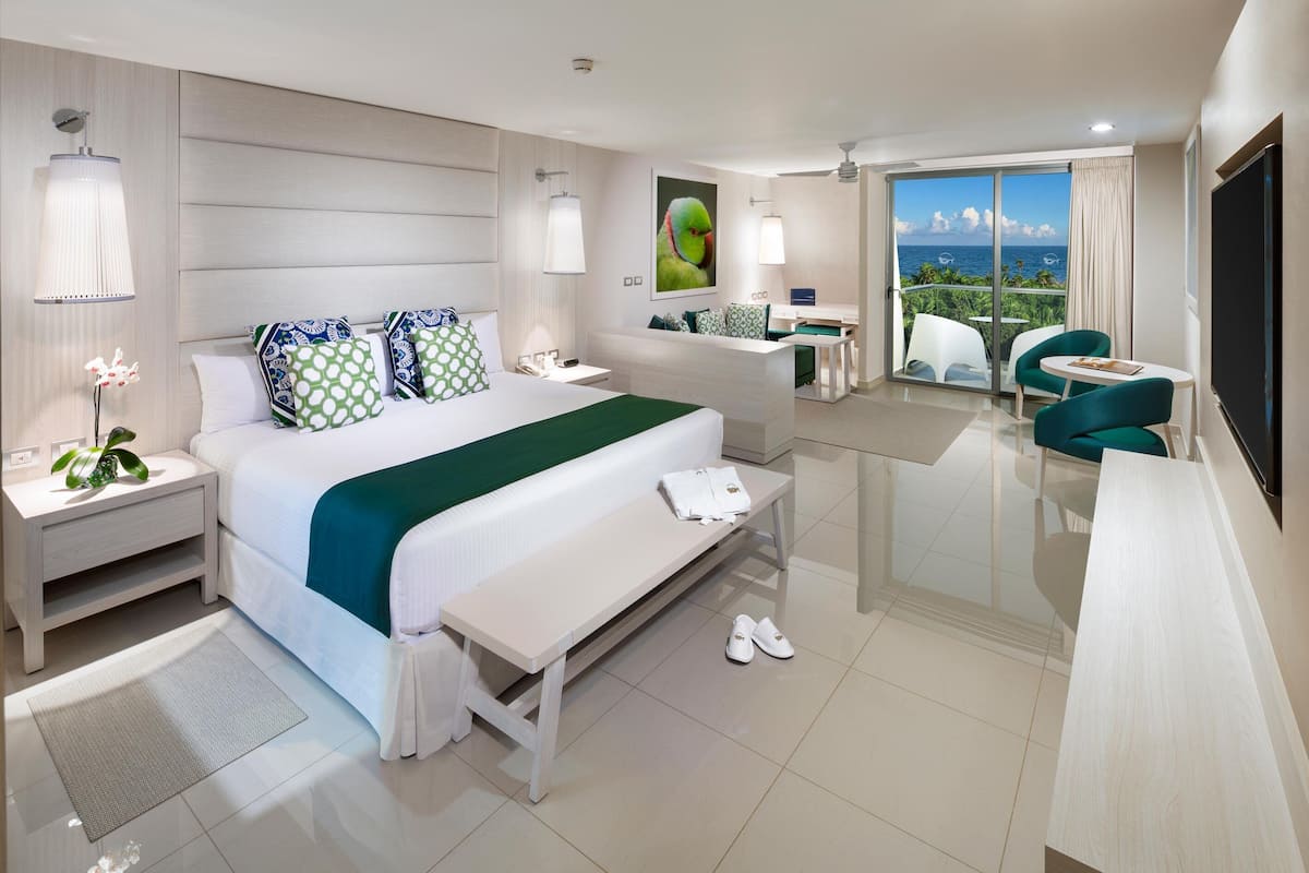A modern hotel room with a large bed, a desk, a balcony with a view, and a TV.