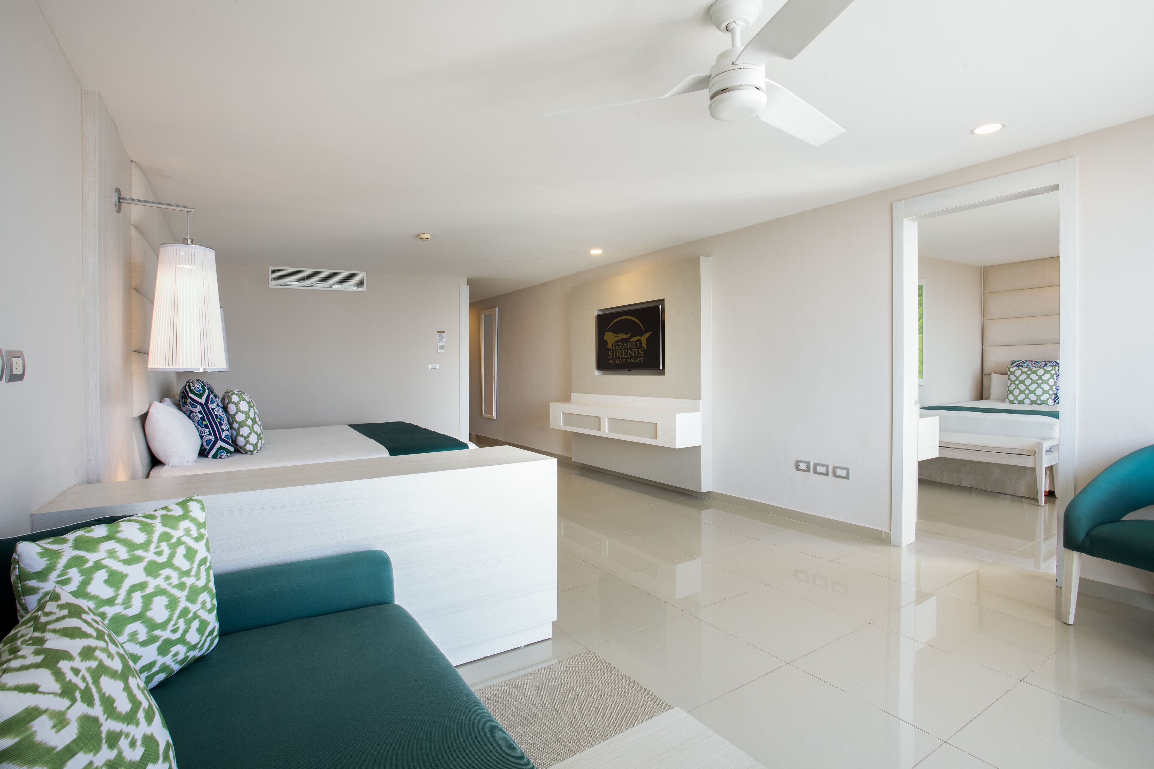 Quarto de hotel moderno com cama, sofá, ventoinha de teto e uma pequena mesa.