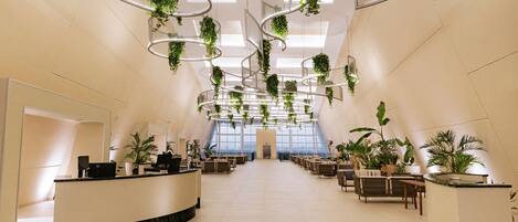 A spacious lobby with a curved reception desk, seating areas, and hanging plants.