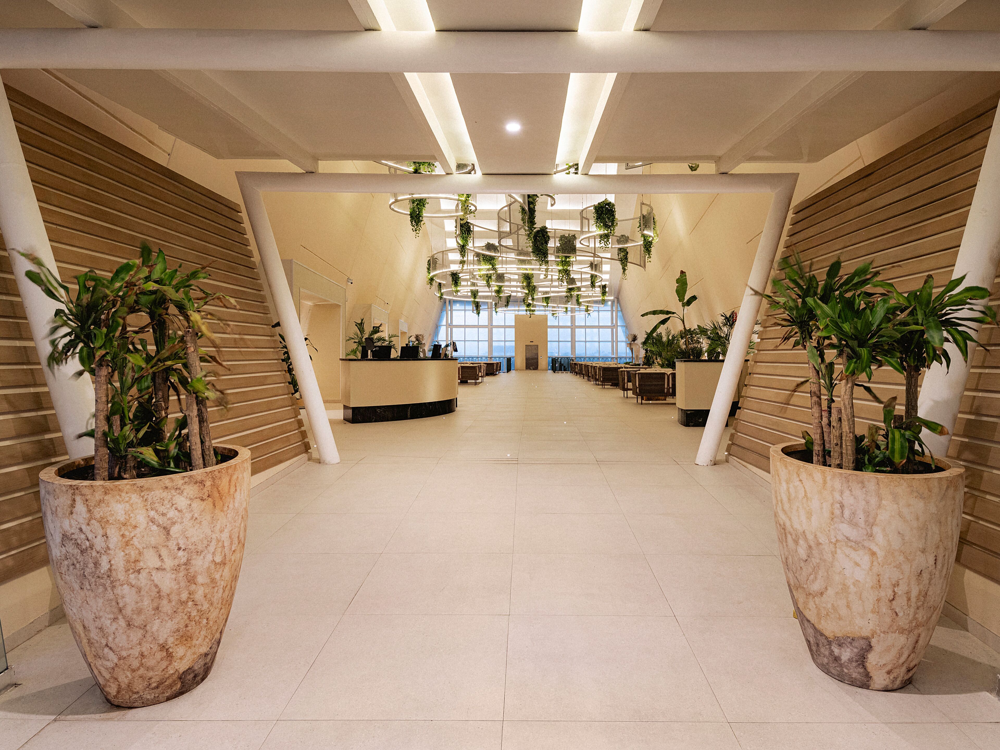 Un vestíbulo amplio con techo alto, grandes plantas en macetas y un mostrador de recepción.