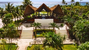 A beachside resort with a thatched-roof structure, a pool, and palm trees. - Grand Sirenis Riviera Maya Resort & Spa - All Inclusive (Akumal)
