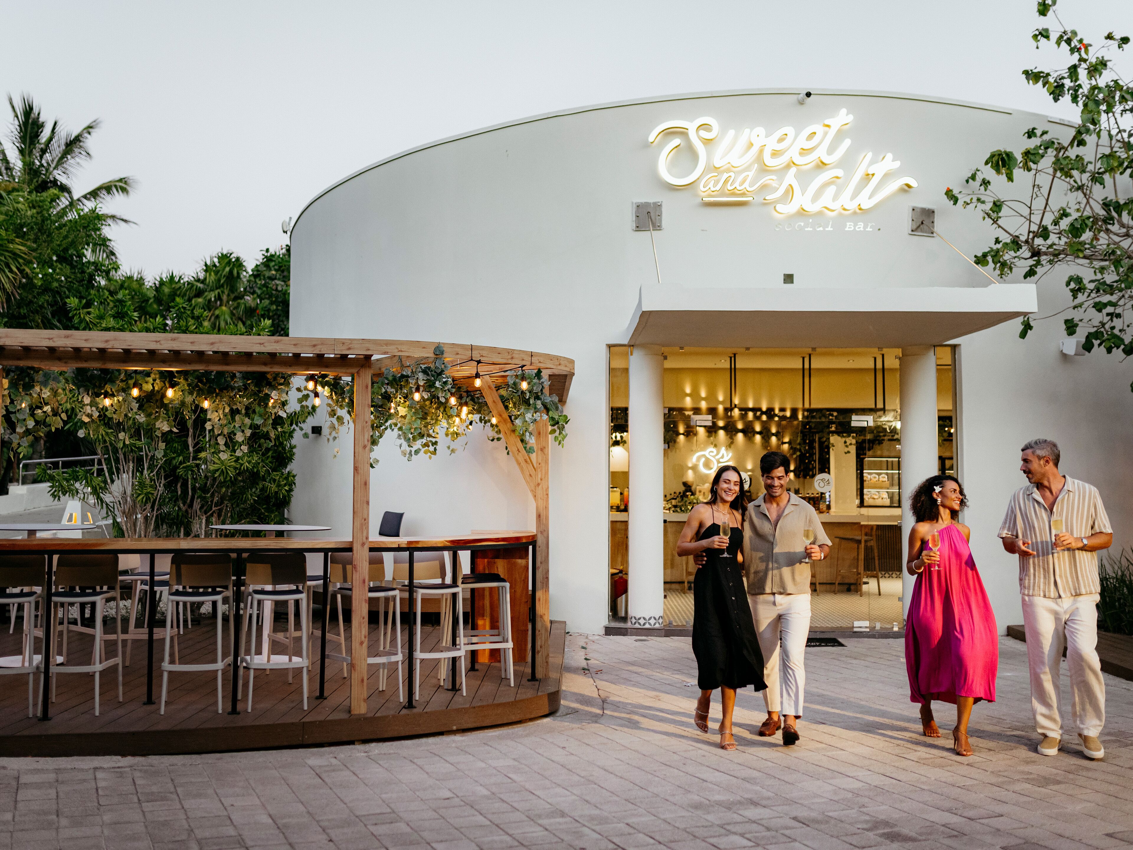 An outdoor seating area with tables and chairs, a wooden pergola, and string lights.