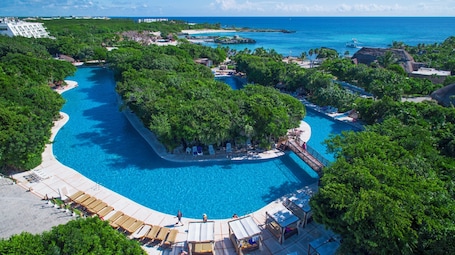A resort with a large central pool surrounded by lush greenery, a smaller pool, and a beach area.