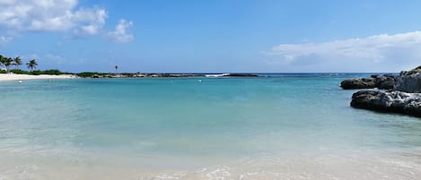 Una playa con agua turquesa cristalina, arena blanca y afloramientos rocosos.