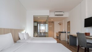 Une chambre d’hôtel avec deux lits, un bureau, une chaise, une télévision et une salle de bain visible à travers une porte en verre.