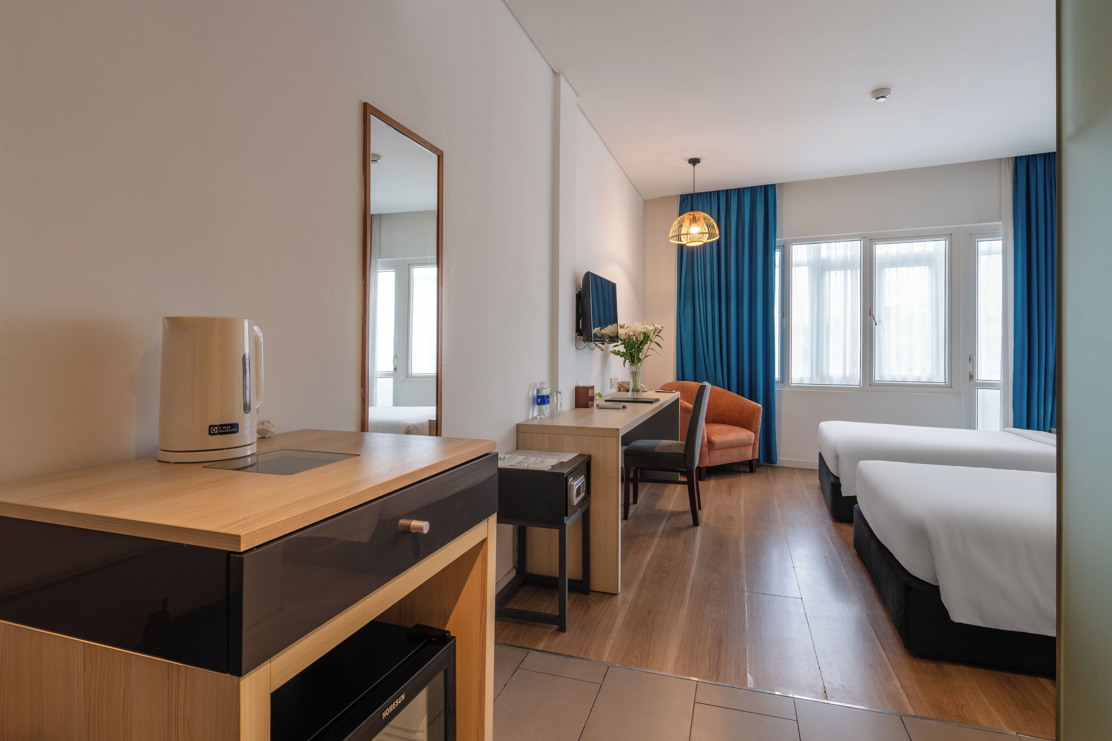 A hotel room with a wooden desk, a chair, a bed, a TV, and a window with curtains.