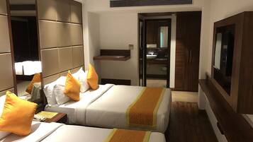 A hotel room with two beds, a TV, a mirror, a bedside table with a lamp, and a bathroom visible through an open door.
