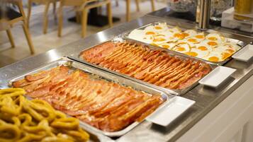 Un bufé con diversas opciones de comida, incluyendo tocino, huevos y pasta.