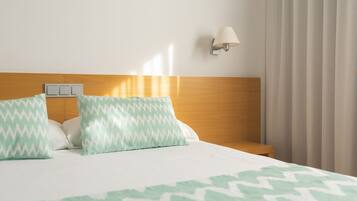 Hotelkamer met een bed, twee kussens, een nachtkastje, een lamp en een raam met gordijnen.