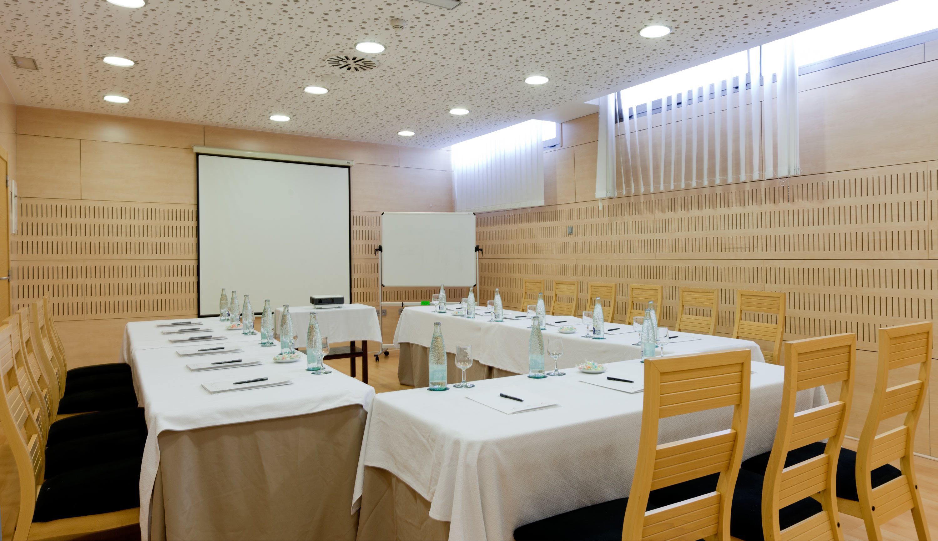 A conference room with tables set for a meeting, equipped with microphones, water bottles, and glassware.