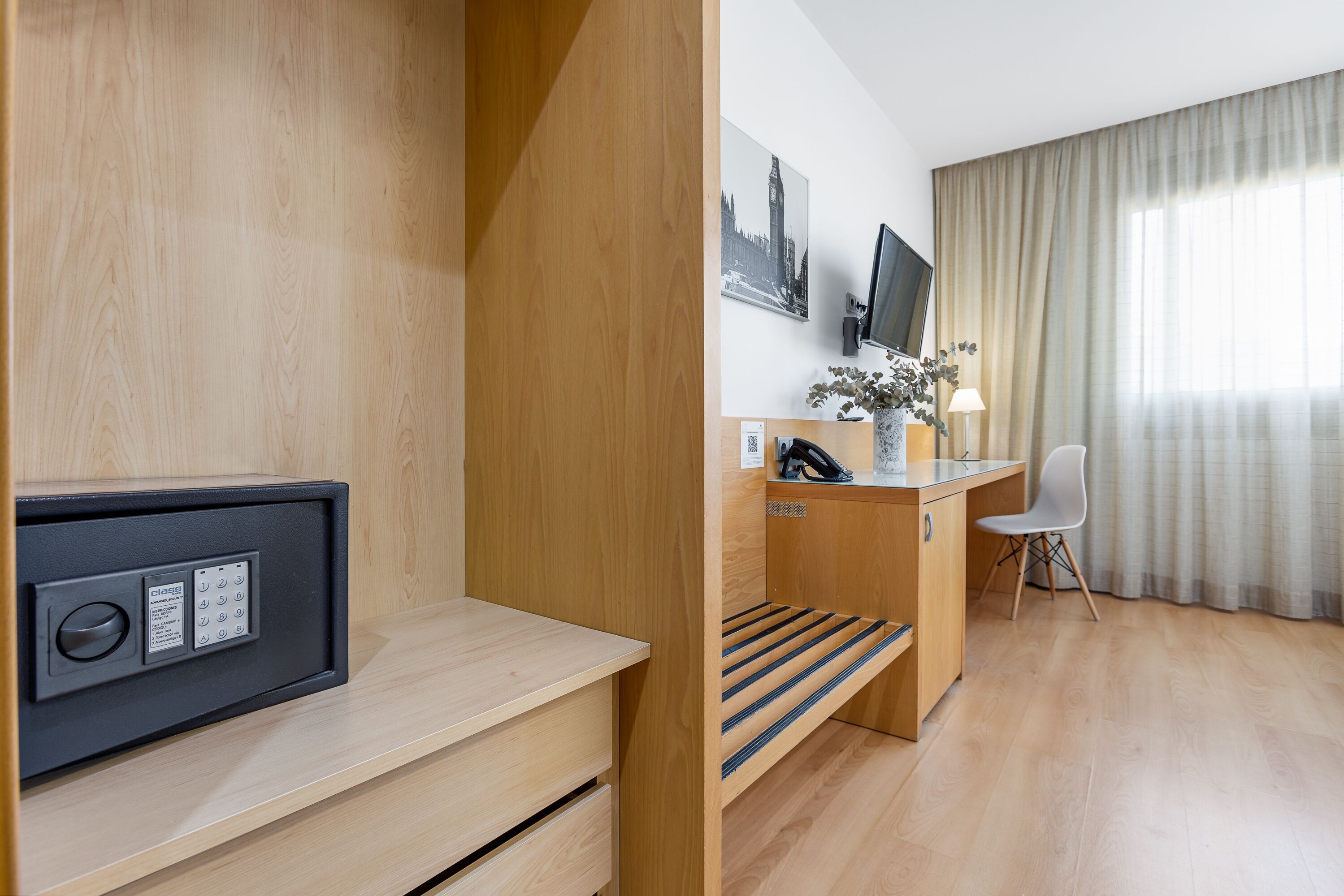 A hotel room with a wooden desk, a chair, a television, a small plant, and a window with curtains.