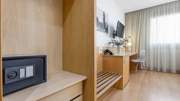 Habitación de hotel con escritorio de madera, una silla, televisor, una planta pequeña y ventana con cortinas.