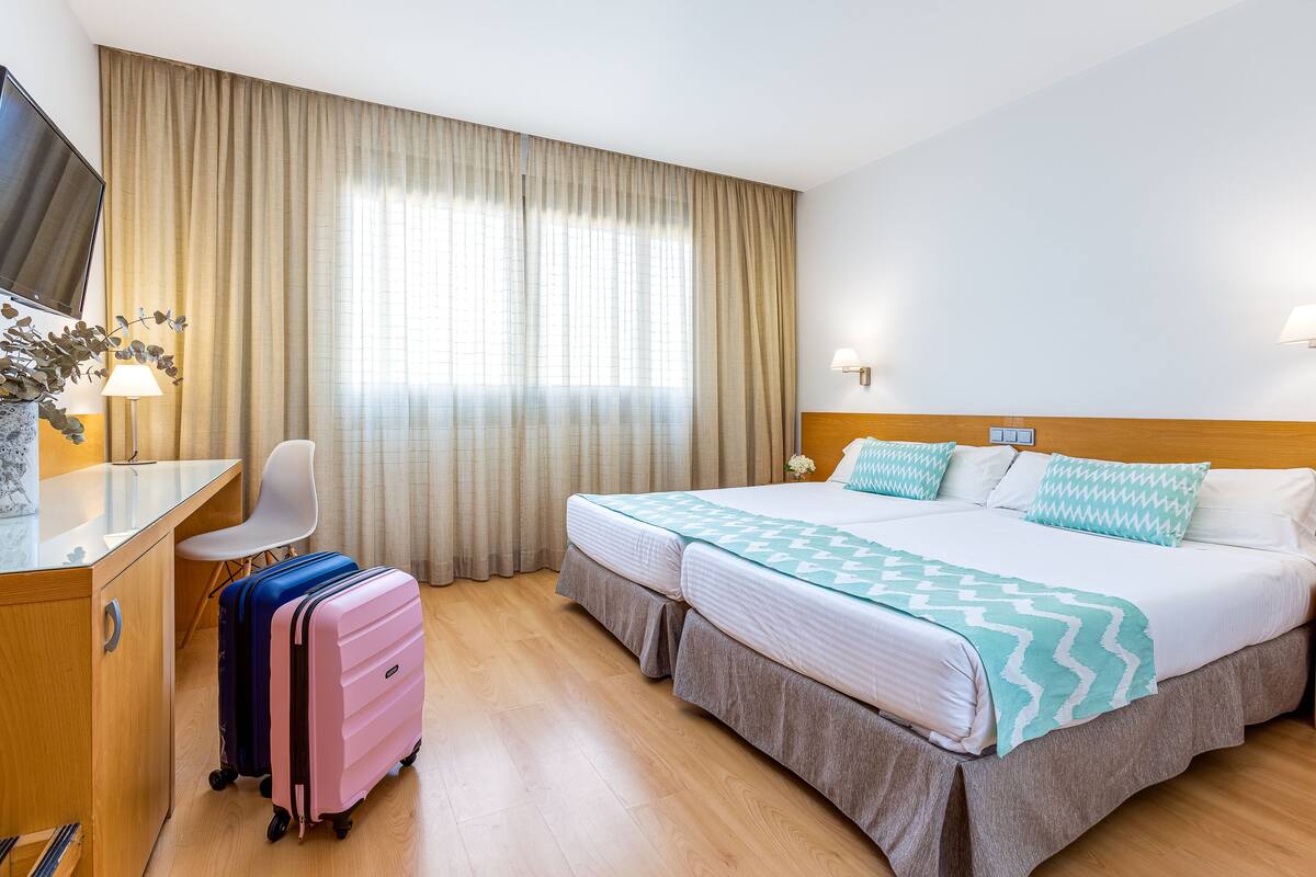 Una habitación de hotel con una cama, un escritorio, una silla y dos maletas.