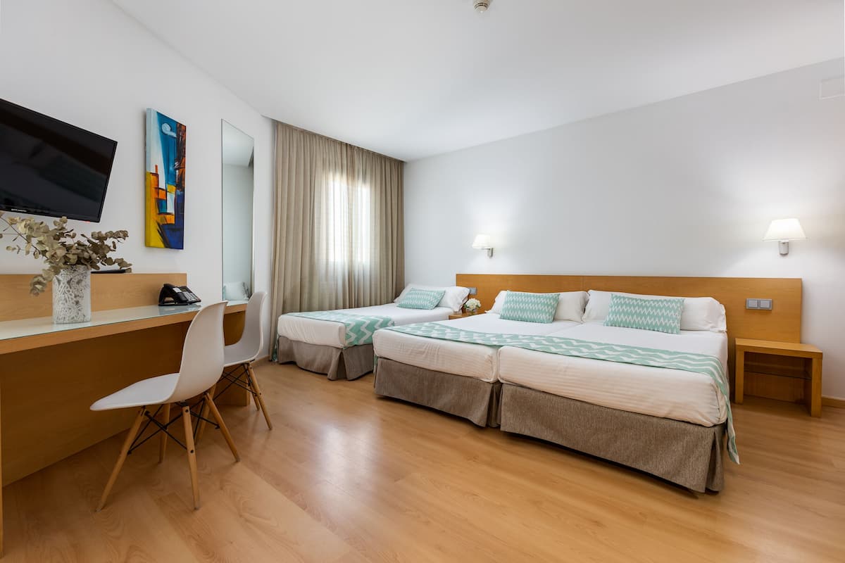 Habitación de hotel con dos camas, un escritorio, una silla, un televisor y un cuadro en la pared.