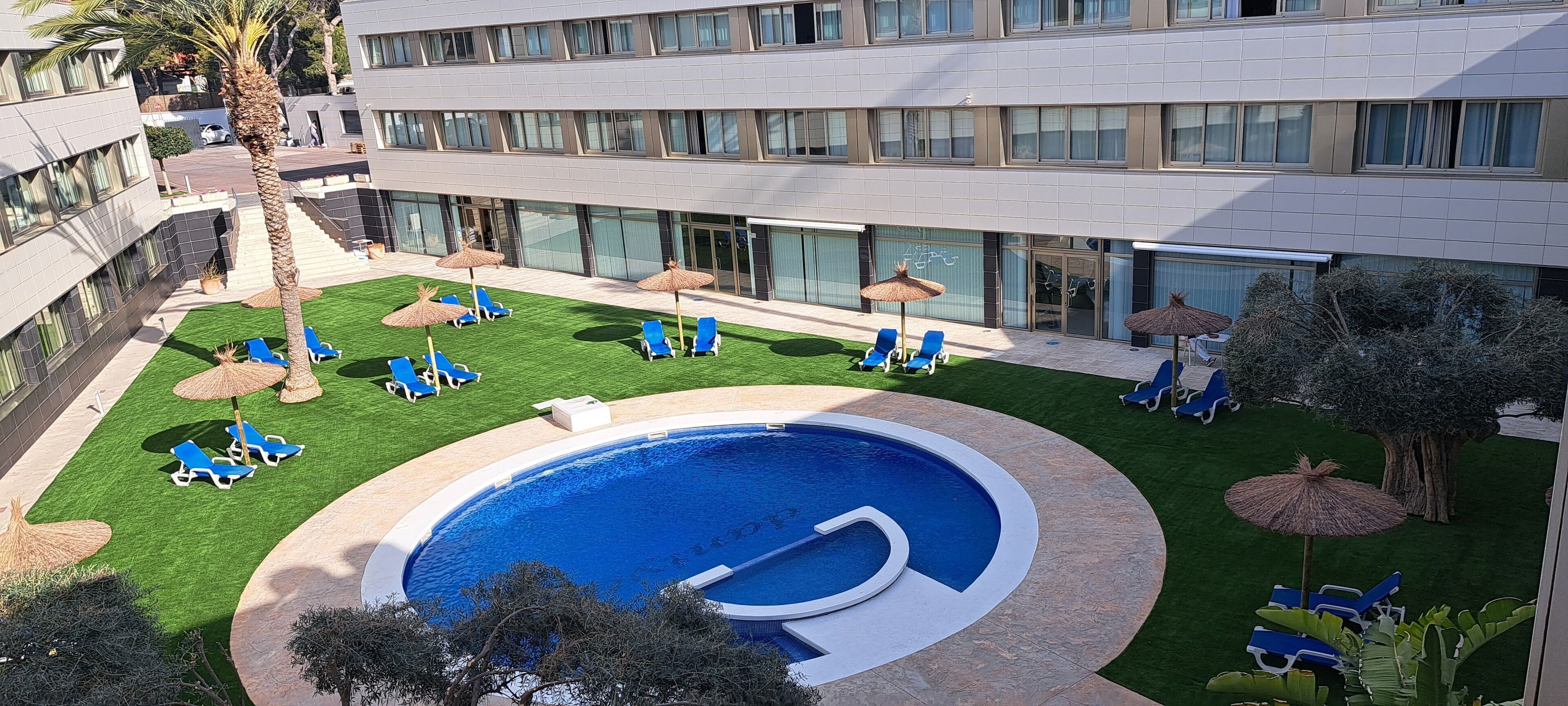 Un patio de hotel con piscina, sillas de descanso y sombrillas.