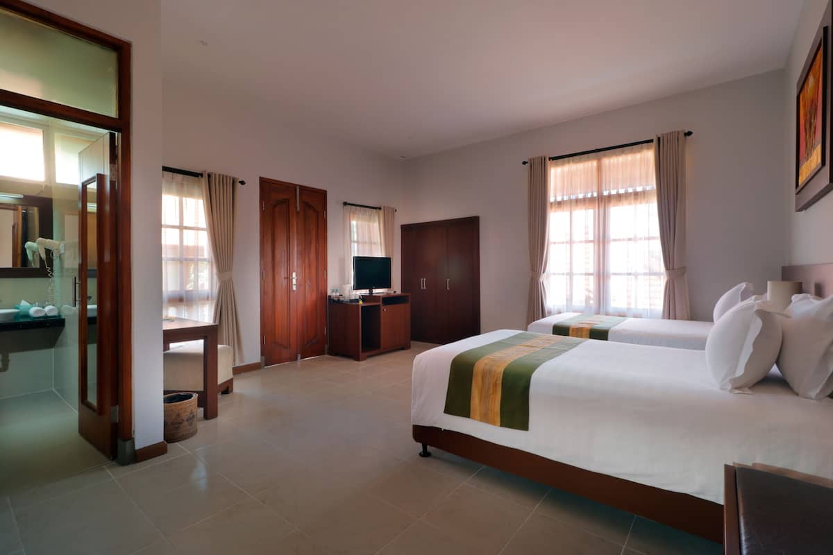 A hotel room with two beds, a TV, a desk, and a bathroom.