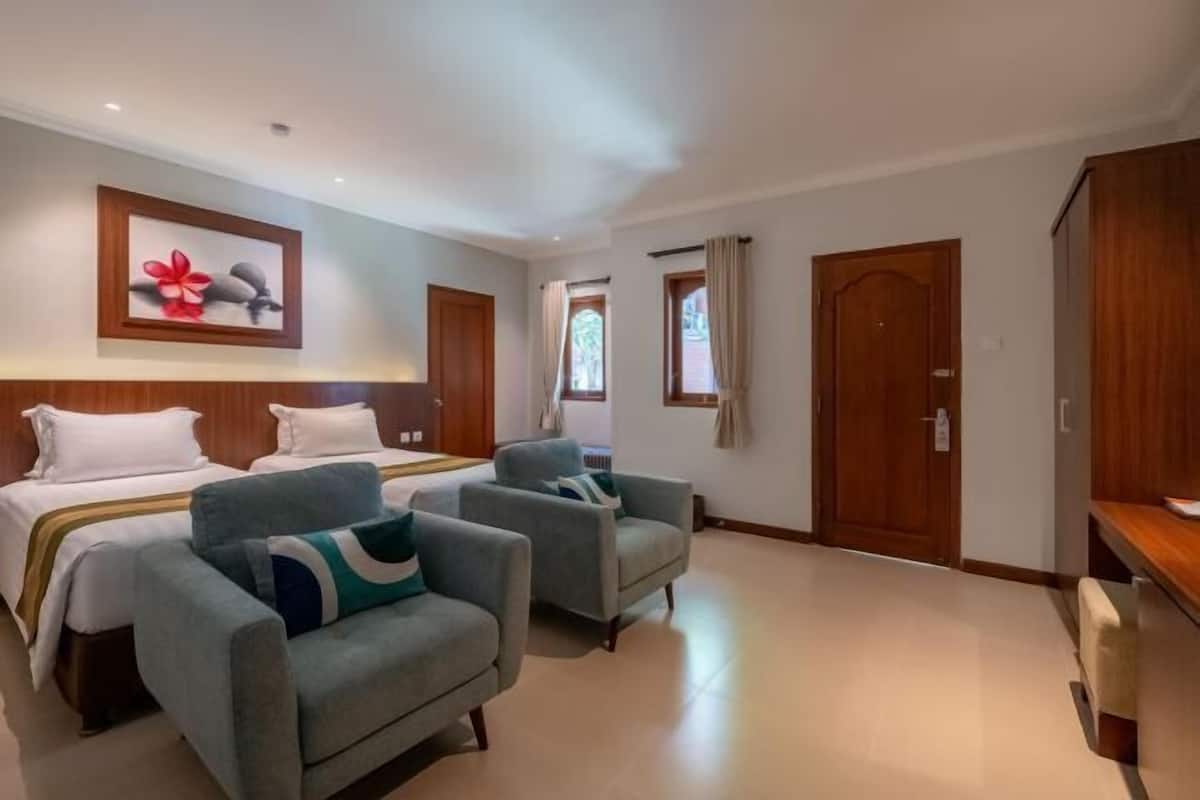 A hotel room with two beds, a sofa, a wooden wardrobe, and a painting on the wall.