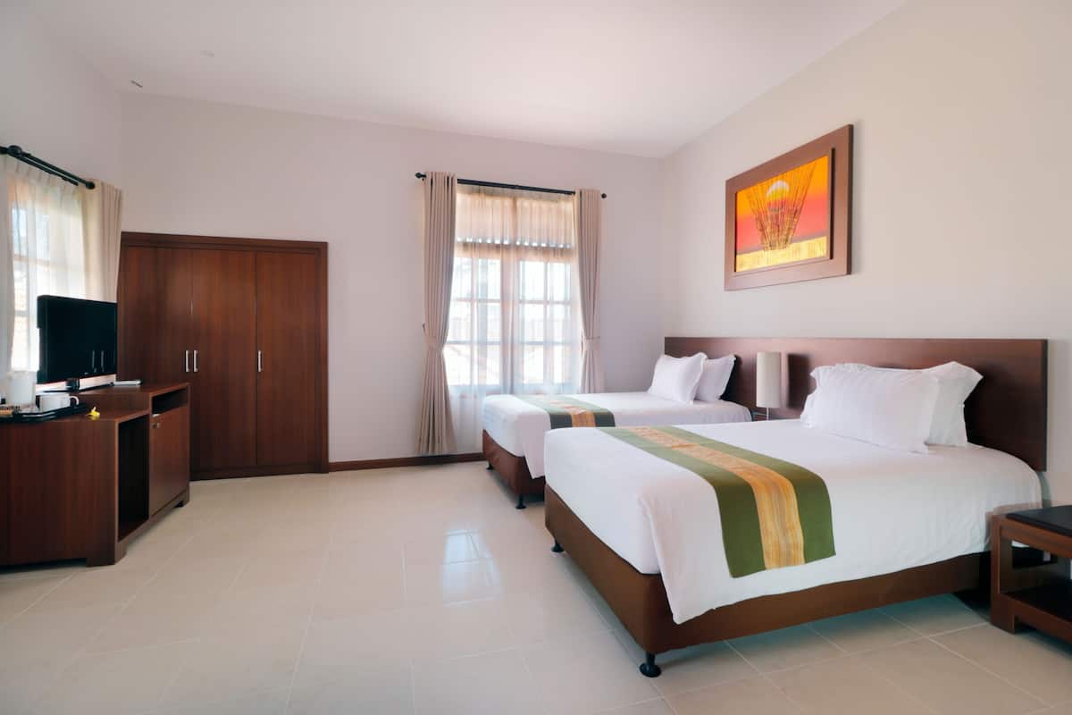 A hotel room with two beds, a desk with a computer, a wardrobe, and a window with curtains.
