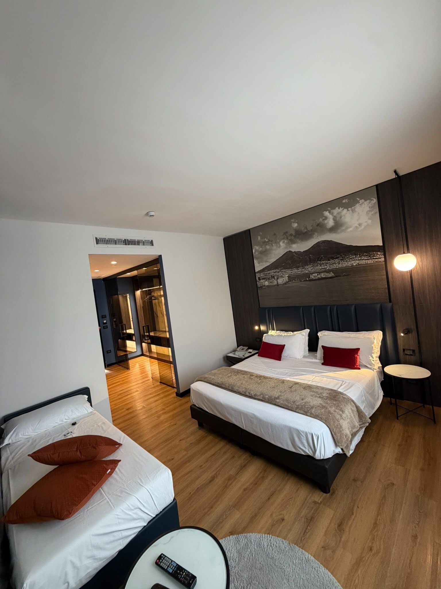 A hotel room with a large bed, a smaller bed, a round table, and a painting of a mountain landscape.