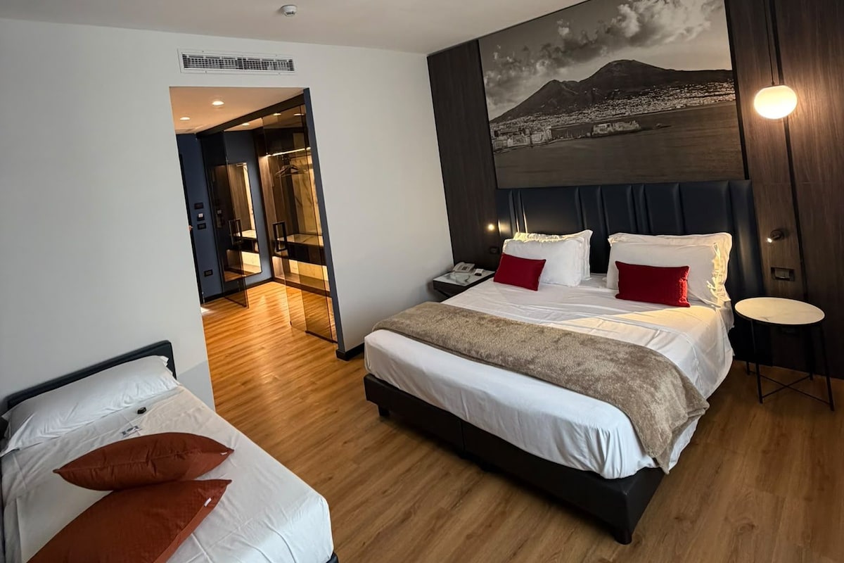 Et hotelværelse med en stor seng, en mindre seng, et rundt bord og et maleri af et bjerglandskab.