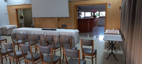A conference room with tables and chairs, a podium, and a large screen. - Hotel Leonessa (Volla)