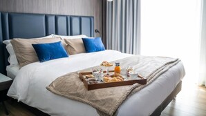 A neatly made bed with a tray of breakfast items, including pastries and a drink, in a modern hotel room with a grey headboard and blue pillows. - Hotel Leonessa (Volla)