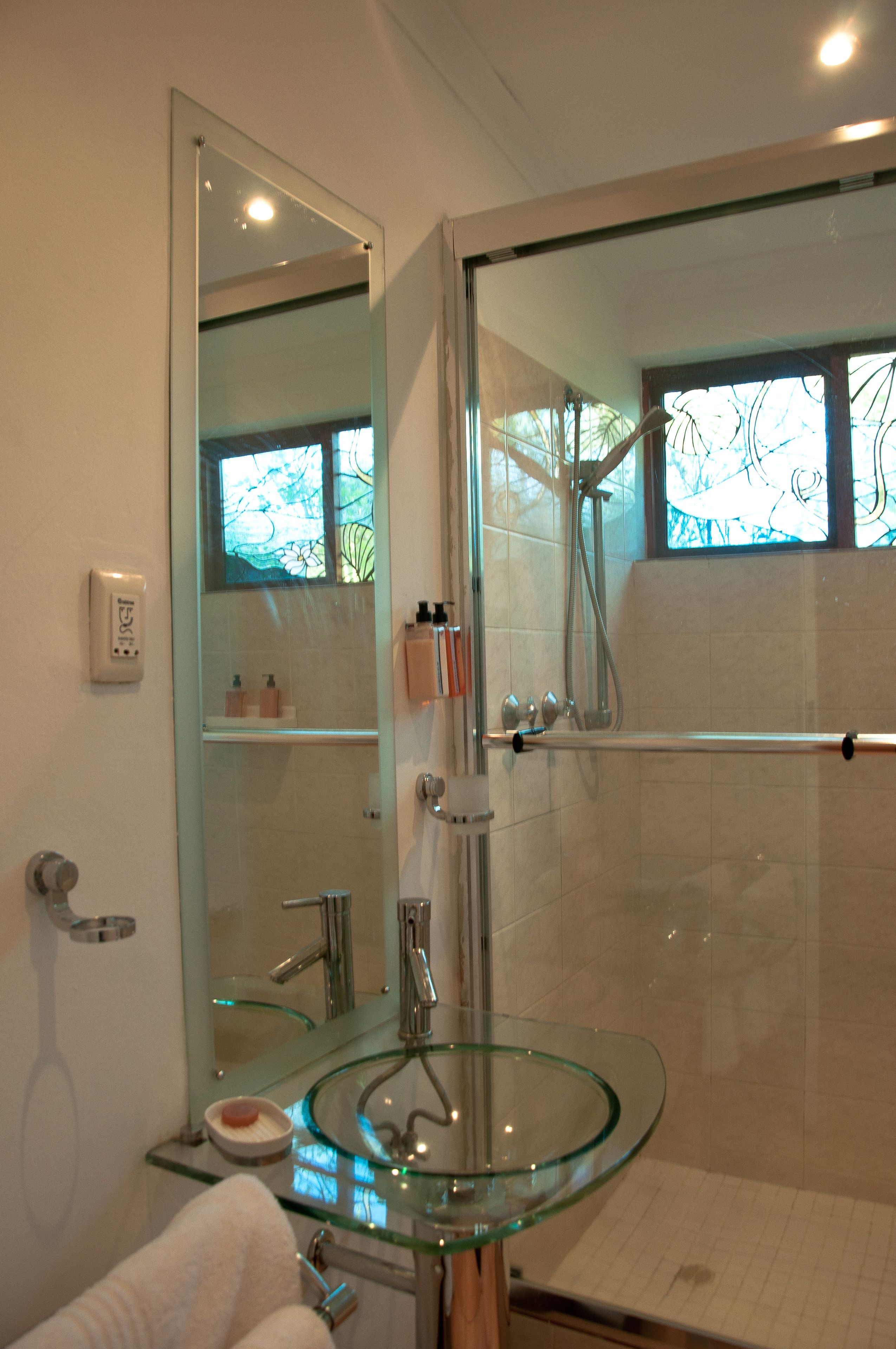 A modern bathroom with a glass sink, a glass shower enclosure, and a large mirror.