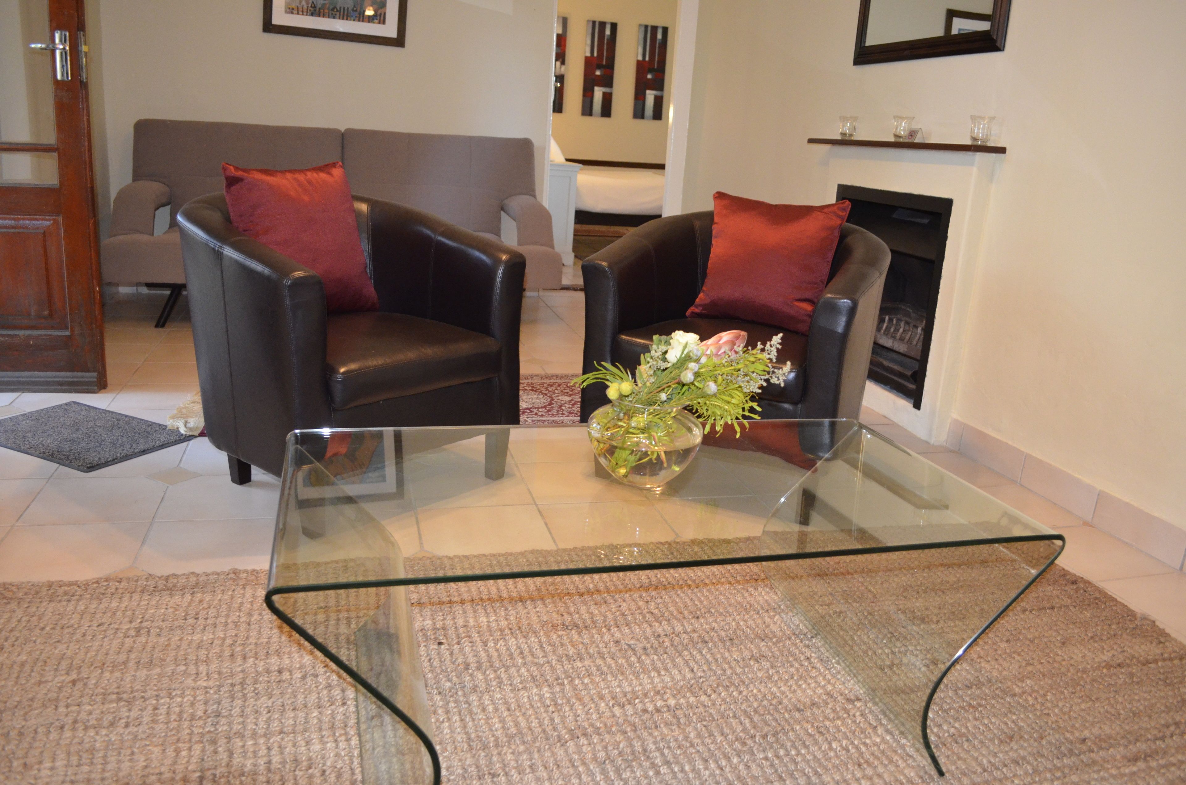 A modern living room with two leather armchairs, a glass coffee table, and a vase of flowers.