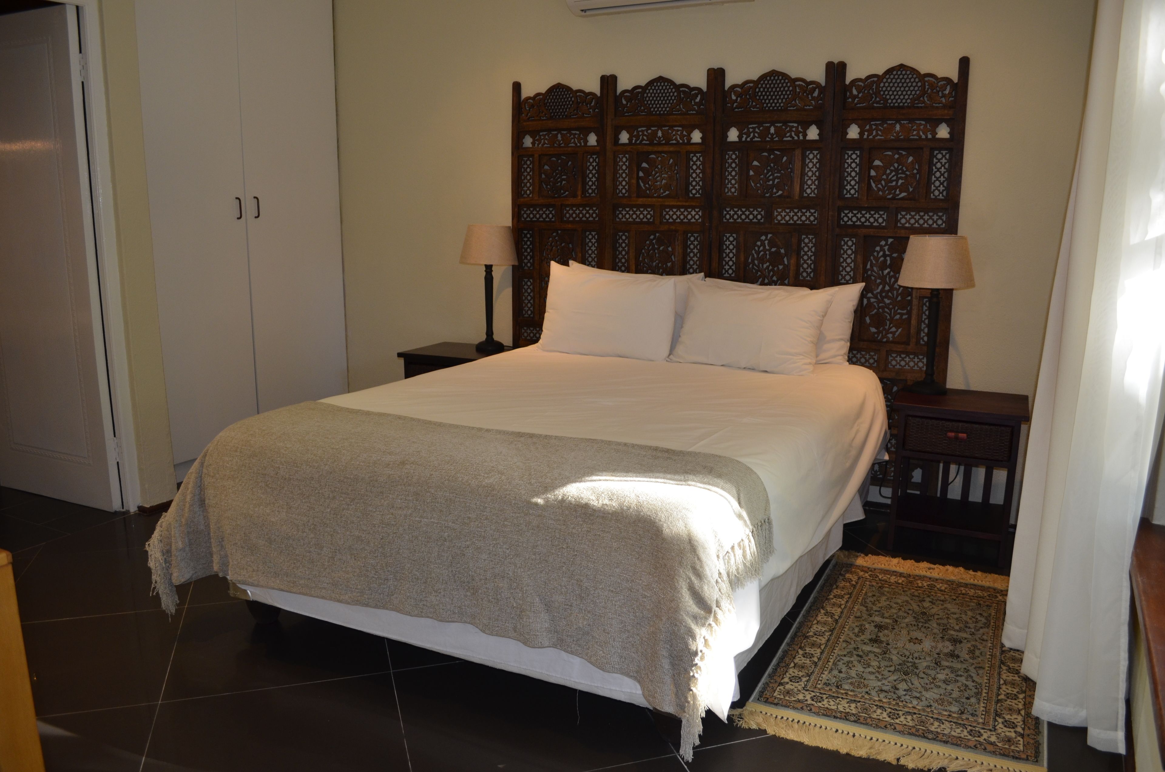 A neatly made bed with a headboard, two bedside tables with lamps, and a patterned rug.
