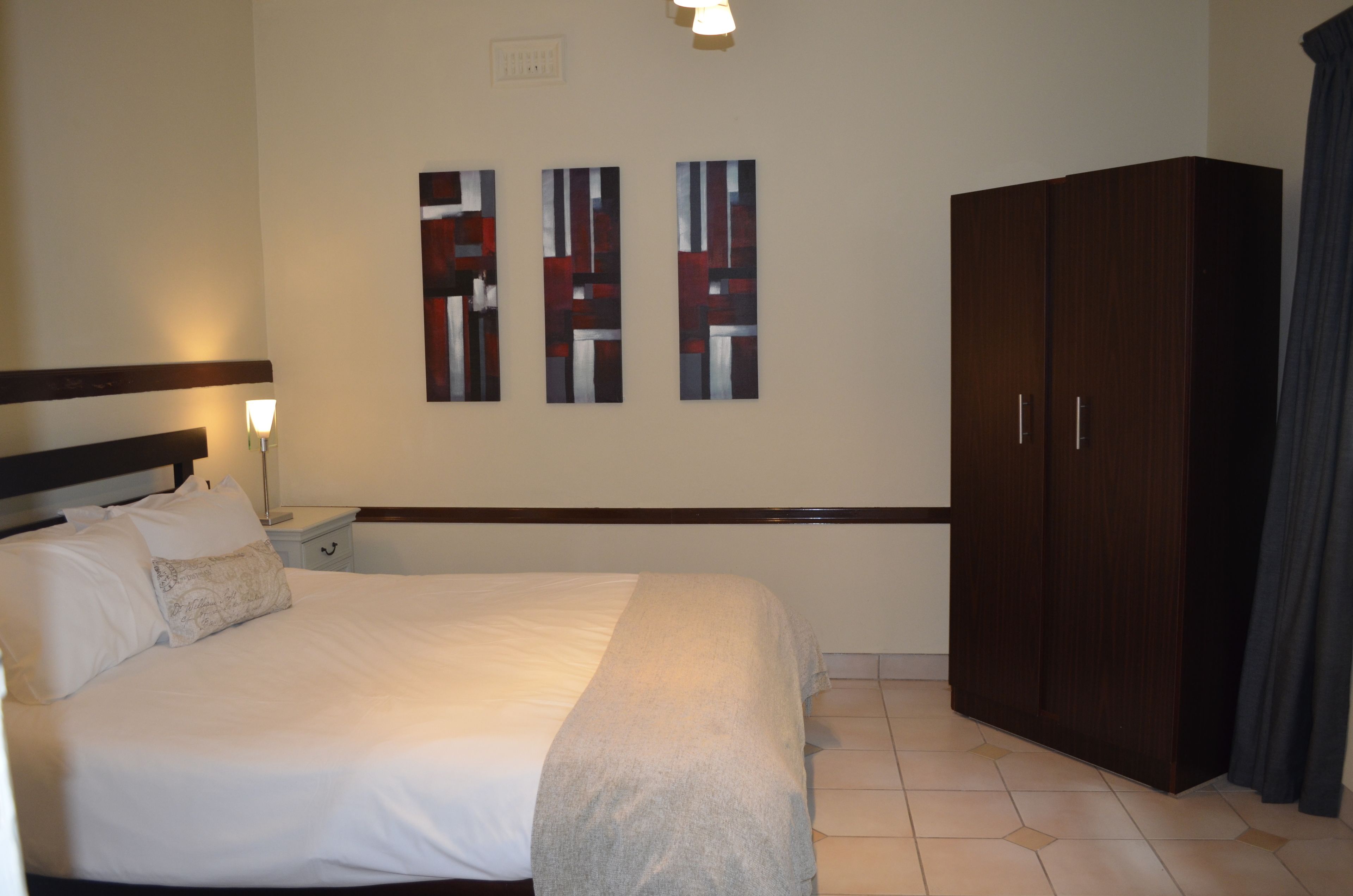 Une chambre d’hôtel comprenant un lit, une table de chevet, une lampe, une armoire et une œuvre d’art abstraite au mur.