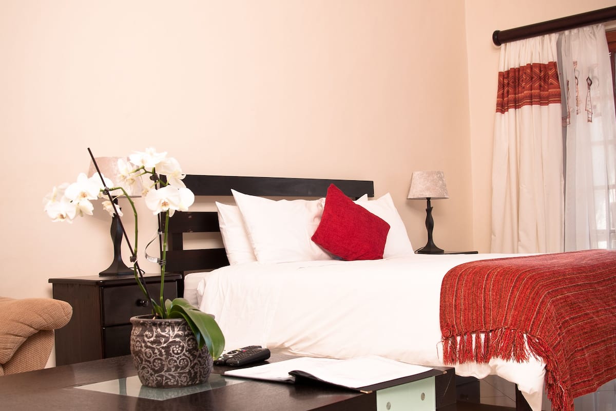 A neatly arranged bedroom with a bed, bedside table, lamp, and a vase with flowers.