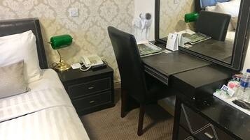 A hotel room with a bed, a desk with a telephone, a chair, a mirror, and a nightstand with a lamp.