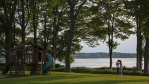 A playground with a slide and a climbing structure, a grassy area, and a lake in the background. - Normanton Park Hotel, BW Signature Collection (Oakham)